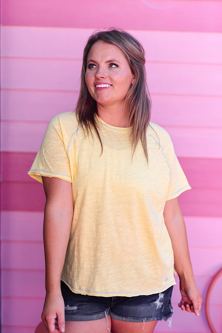 Woman wearing a yellow t-shirt and denim shorts against a pink background