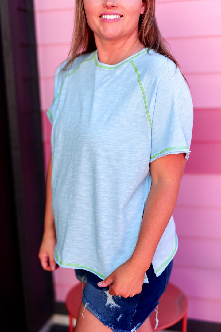 Light blue short-sleeve women's top with green stitching and a relaxed fit, perfect for casual outings.