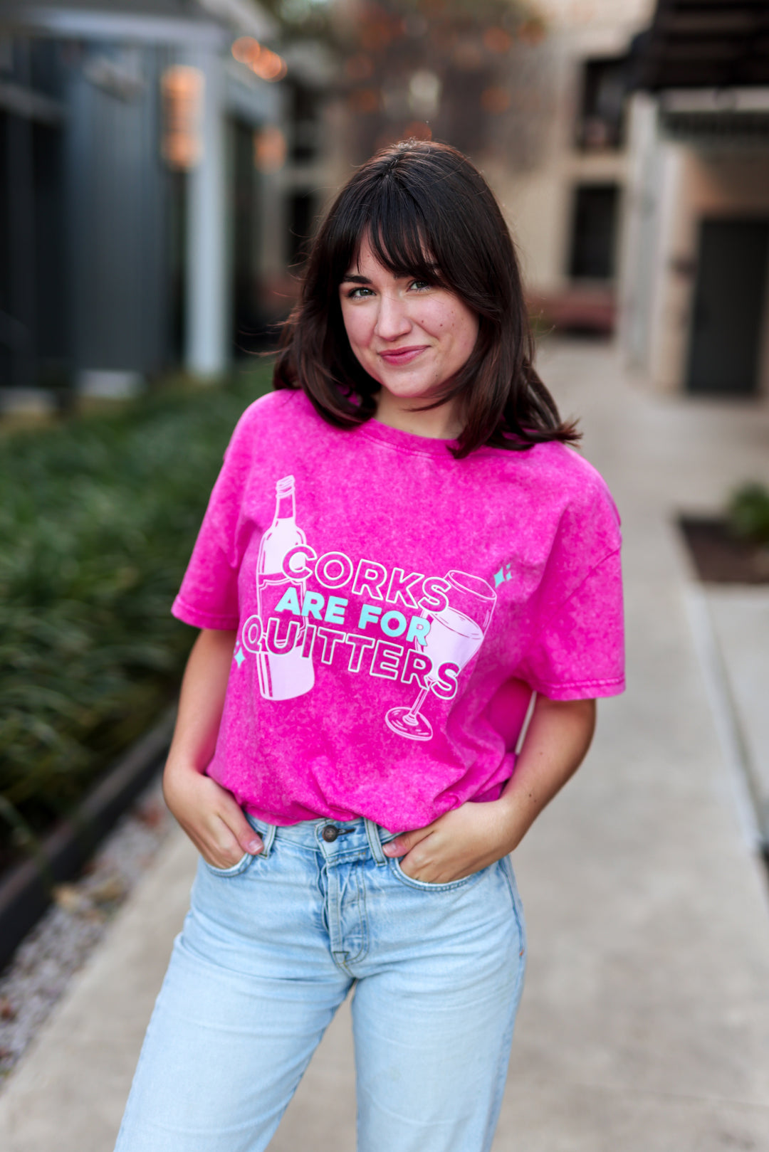 Person wearing a pink t-shirt with text and graphics, standing outdoors.