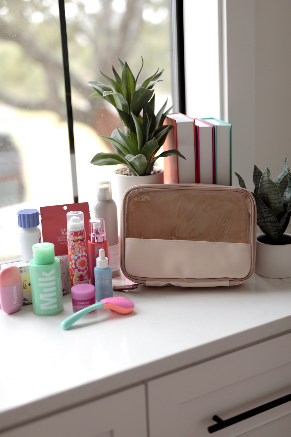 Stylish beige cosmetic bag with transparent front, surrounded by skincare products on a counter.