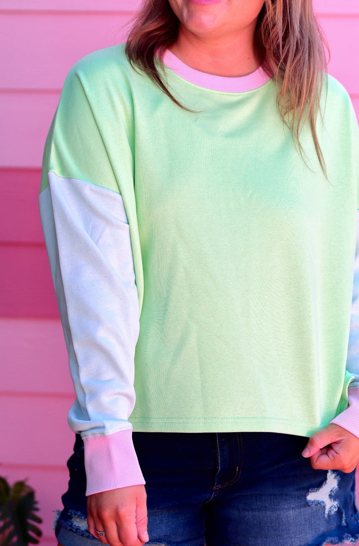 Woman wearing a light green sweatshirt with blue sleeves against a pink wall.