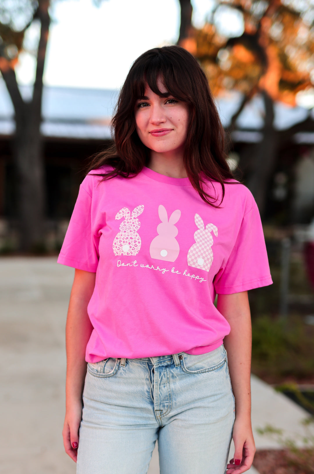Person wearing a pink t-shirt with white graphics and text, standing outdoors.