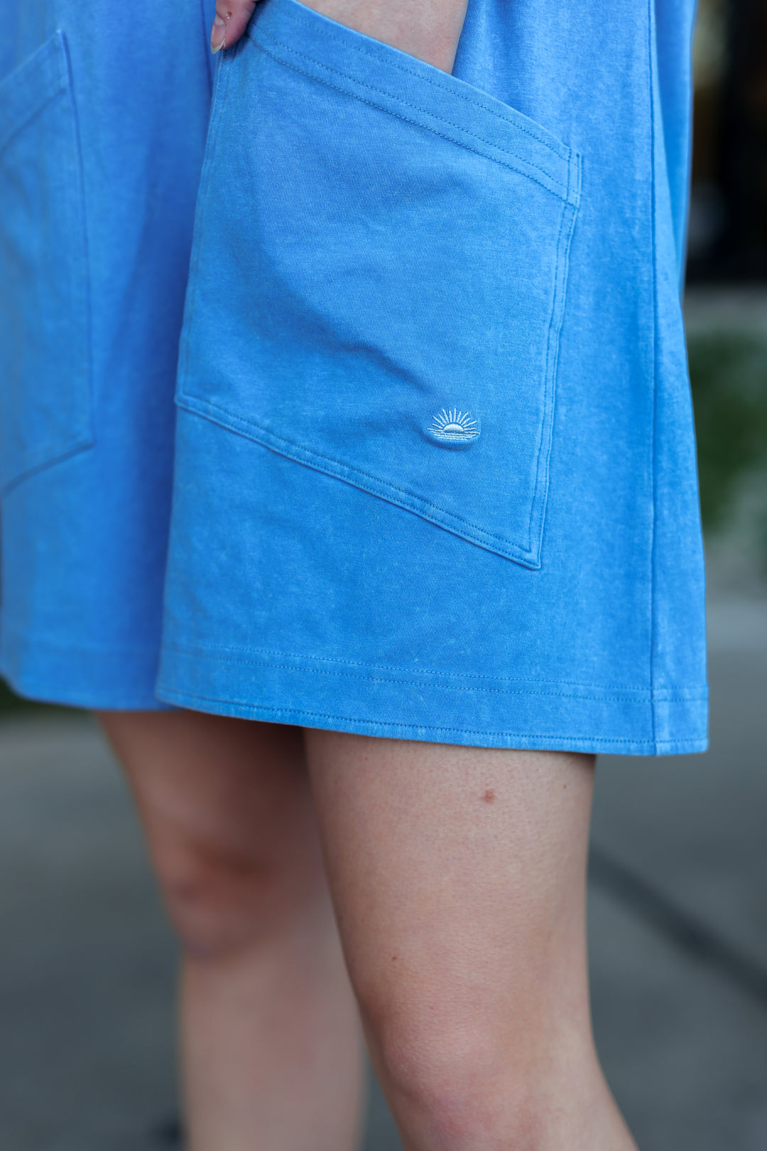 Light blue casual dress featuring large pockets and an embroidered sun logo on side.