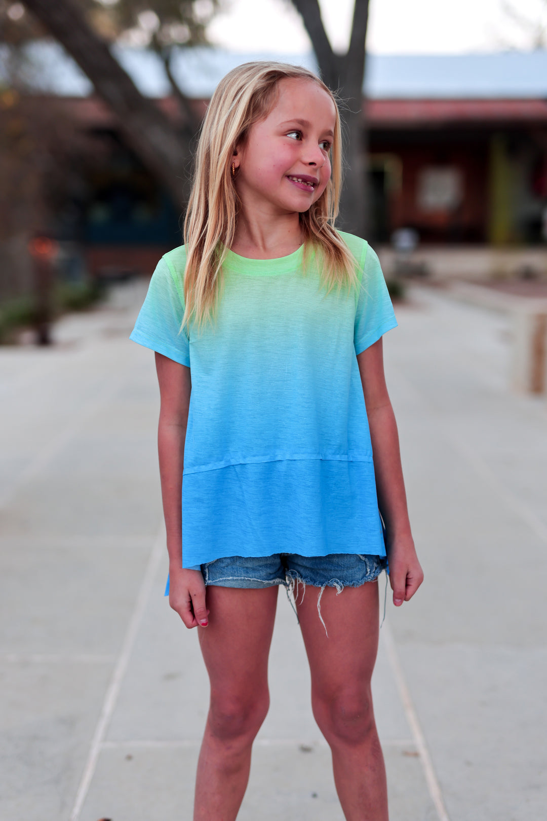 Young girl wearing a blue and green ombre t-shirt outdoors.