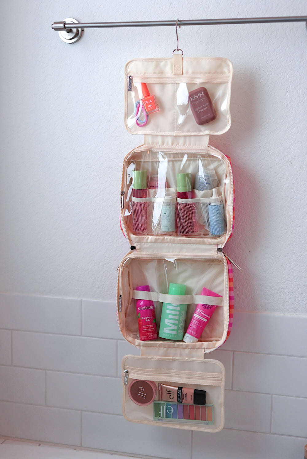 Hanging cosmetic organizer in soft pink, featuring multiple clear compartments for skincare and makeup products.