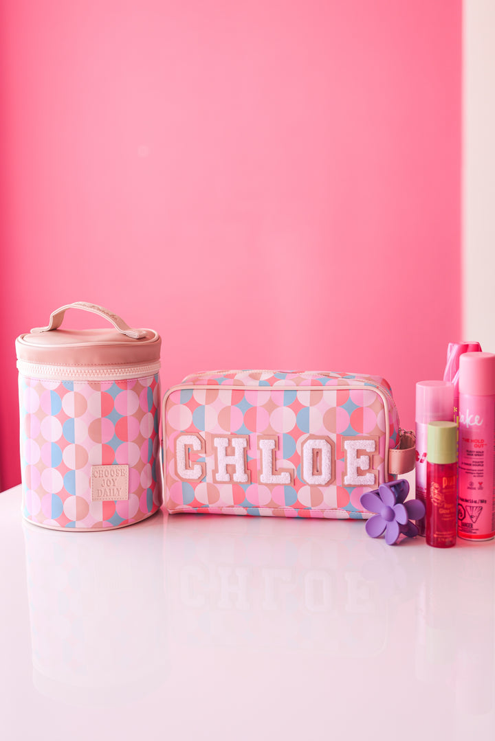 Colorful pink cosmetic bags with 'CHLOE' embroidery and accessories on a reflective surface.