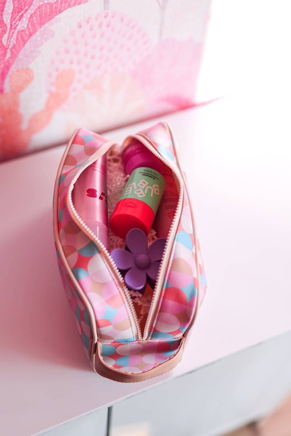 Colorful cosmetic bag with pink and blue polka dots, featuring beauty products and a flower accessory inside.