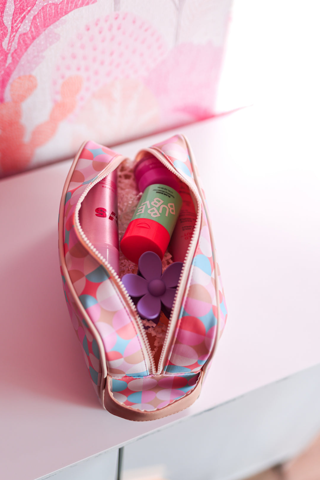 Colorful cosmetic bag with pink and blue polka dots, featuring beauty products and a flower accessory inside.