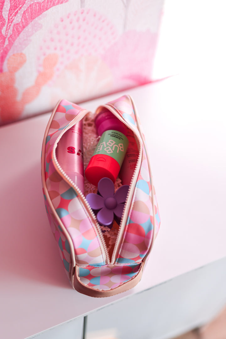Colorful cosmetic bag with pink and blue polka dots, featuring beauty products and a flower accessory inside.