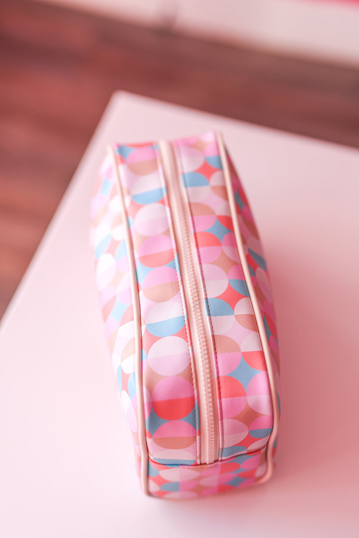 Colorful patterned cosmetic bag in pink, blue, and cream, featuring a zipper closure and stylish design.