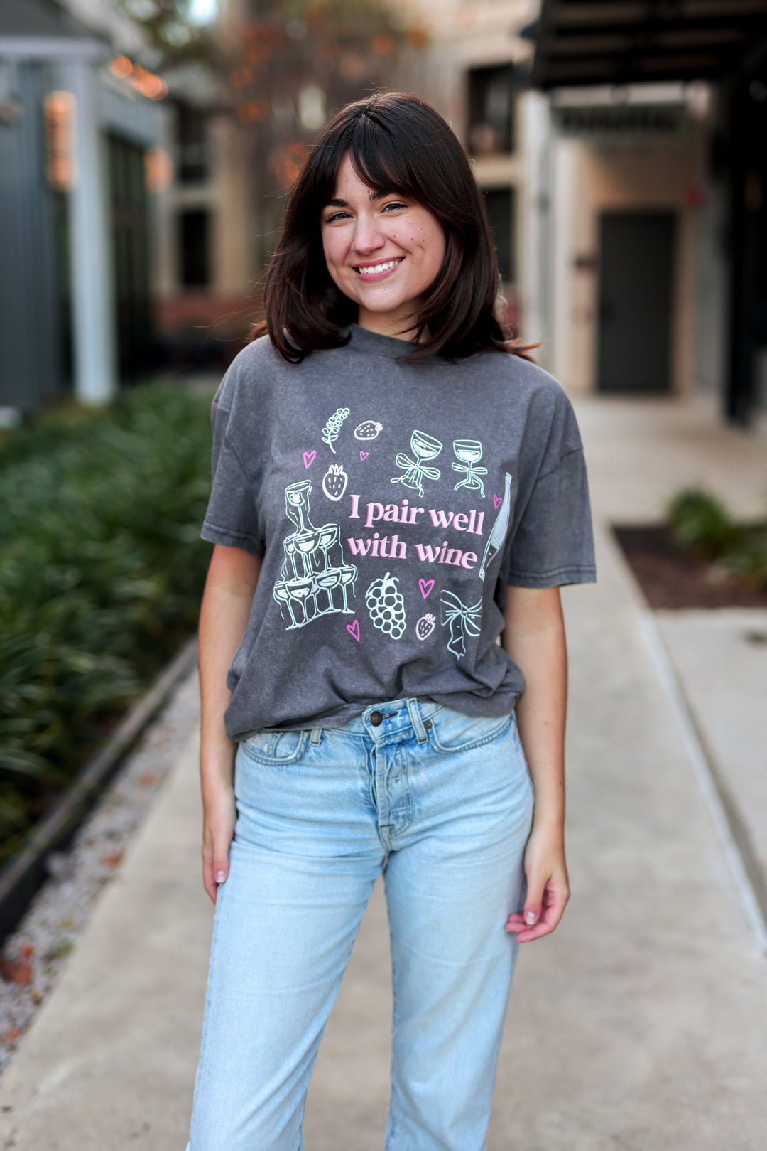 Person wearing a gray t-shirt with wine-themed graphics and text, standing outdoors.