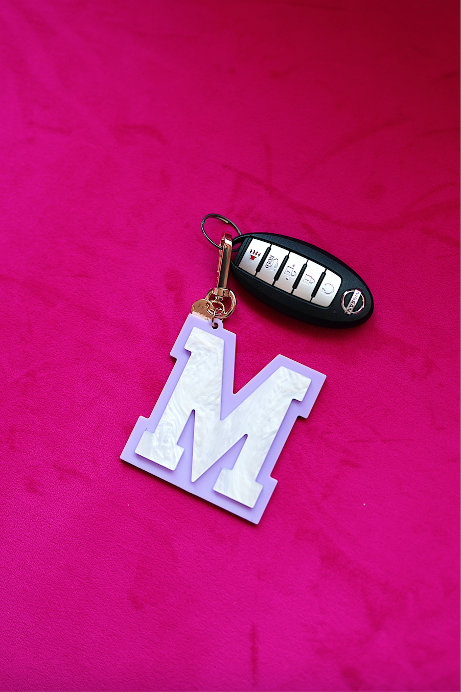 Personalized purple letter 'M' keychain with a pearlescent finish on a pink background.