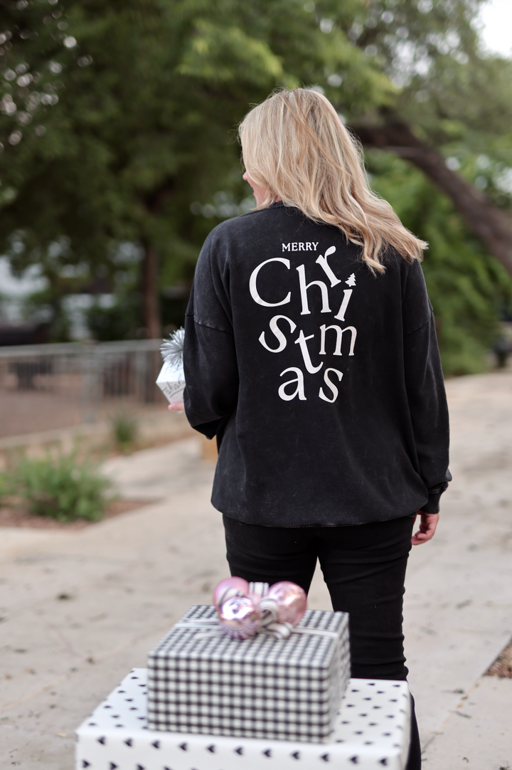 Black Merry Christmas sweatshirt in a casual outdoor setting, featuring bold typography and relaxed fit.