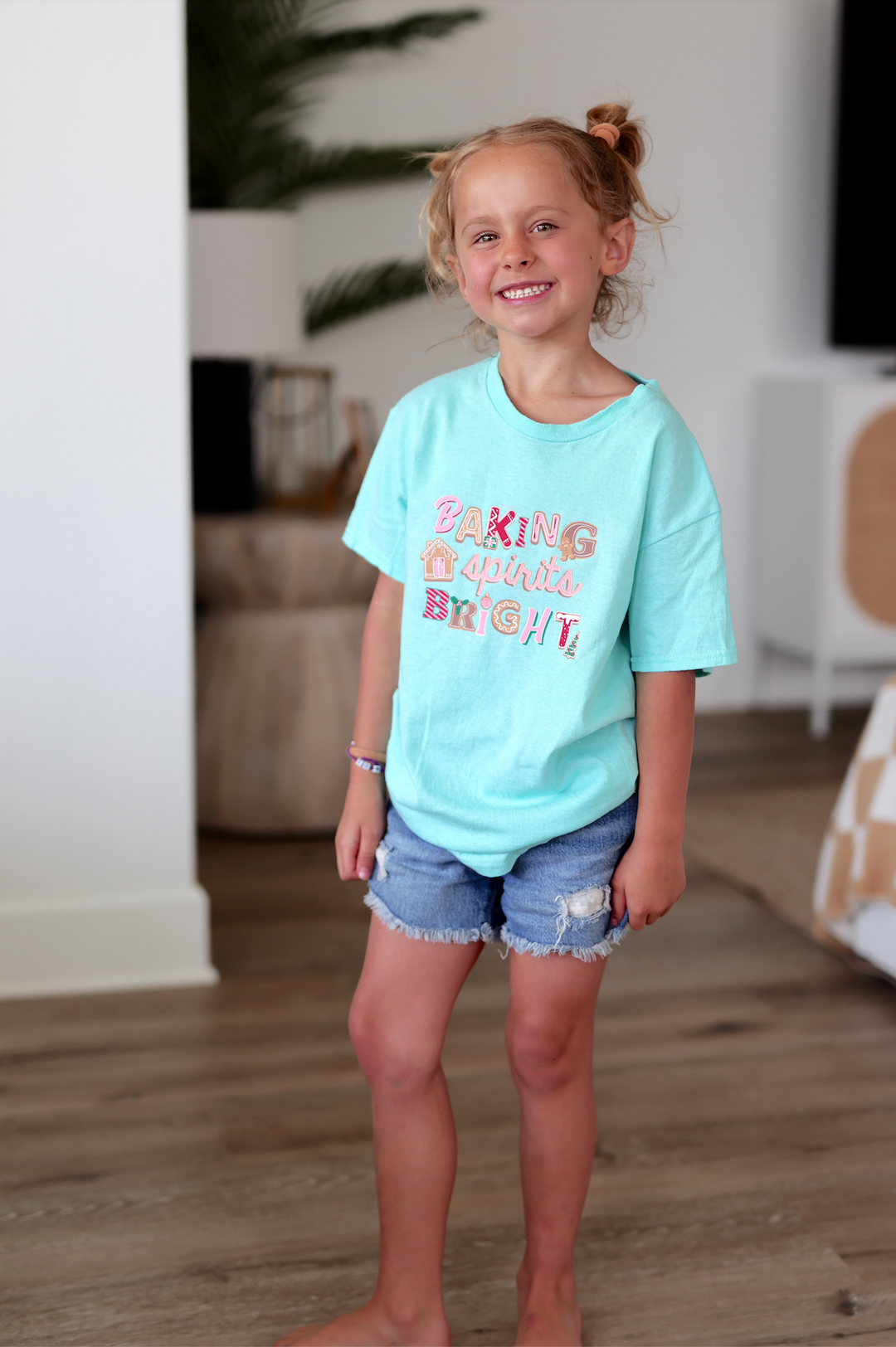 Mint green children's t-shirt with 'Baking spirits bright' design and denim shorts.