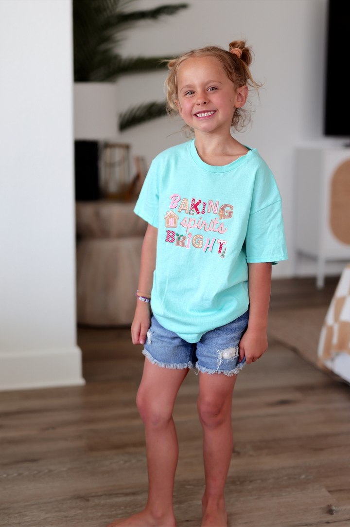 Mint green children's t-shirt with 'Baking spirits bright' design and denim shorts.