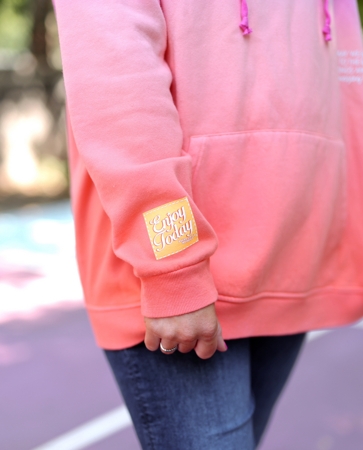 Light pink hoodie with 'Enjoy Today' patch, featuring drawstrings and a cozy kangaroo pocket.
