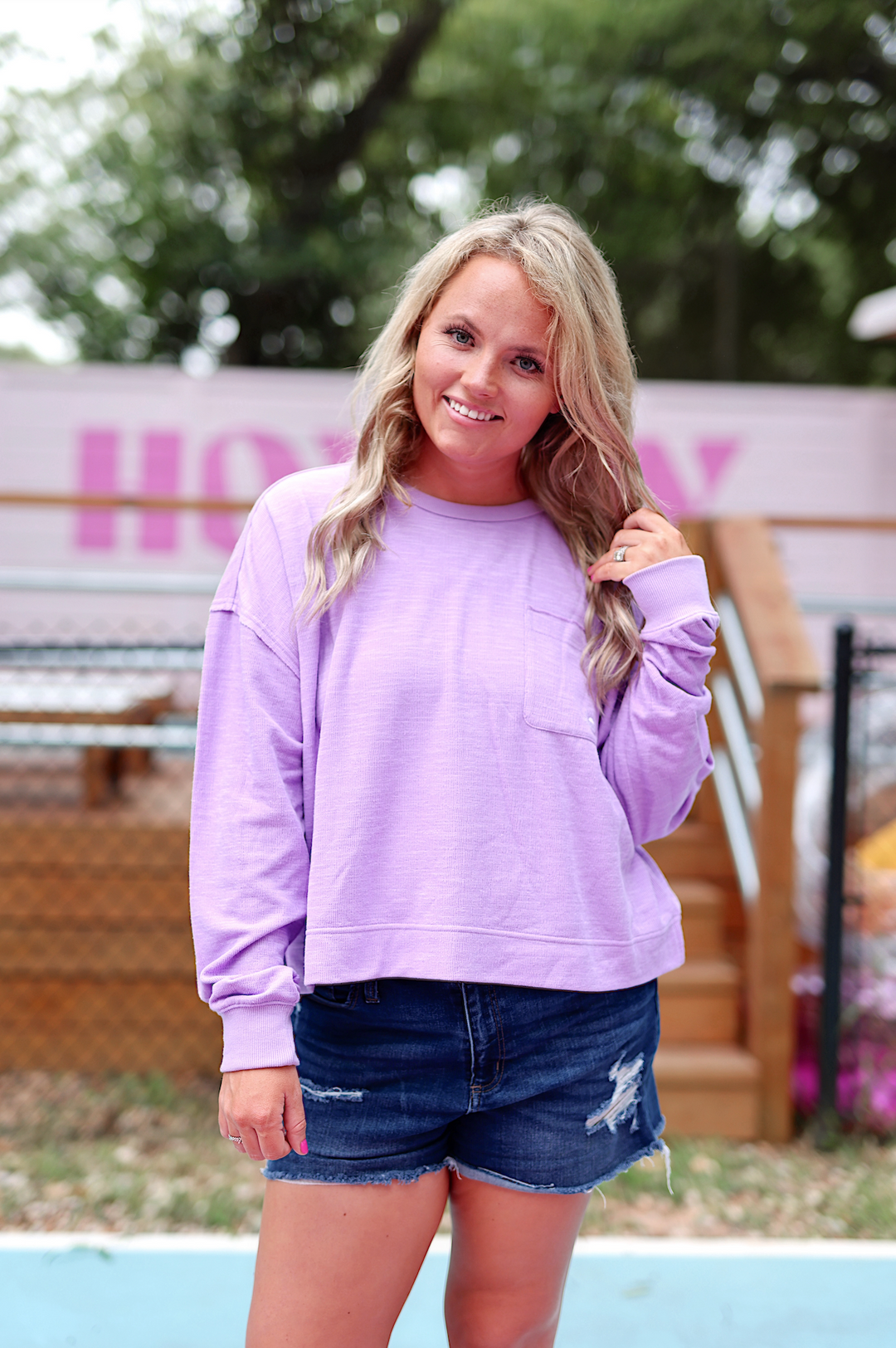 Stylish lavender long-sleeve top with pocket, paired with distressed denim shorts.