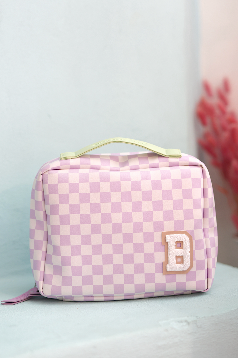 Pink checkered cosmetic bag with a handle and a decorative 'B' patch, perfect for makeup essentials.