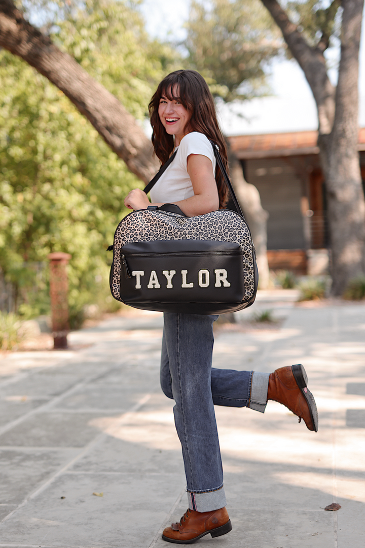 Stylish leopard print bag with 'TAYLOR' text, black leather accents, ideal for travel or daily use.