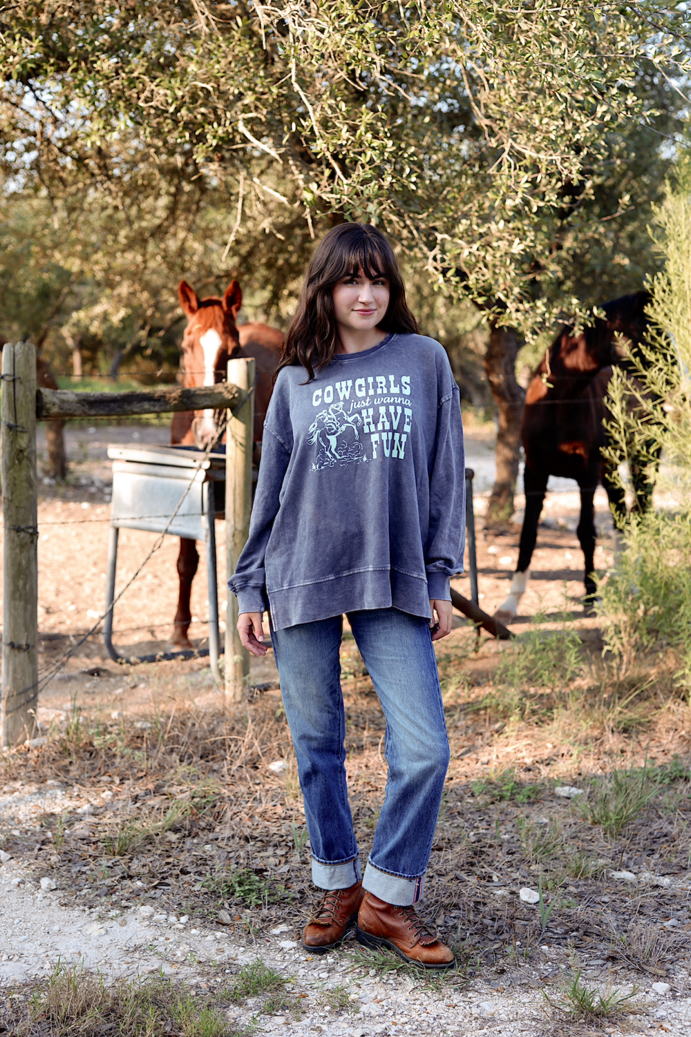 Cozy gray cowgirl sweatshirt with fun graphic, paired with blue jeans and brown boots in a rustic outdoor setting.