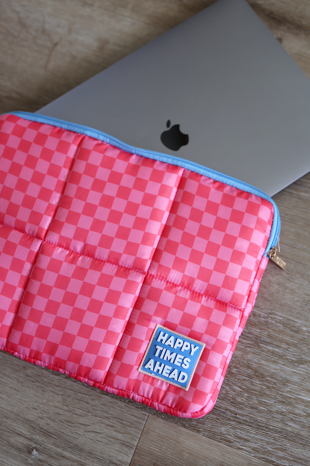 Pink checkered laptop sleeve with 'HAPPY TIMES AHEAD' patch, padded for protection and style.