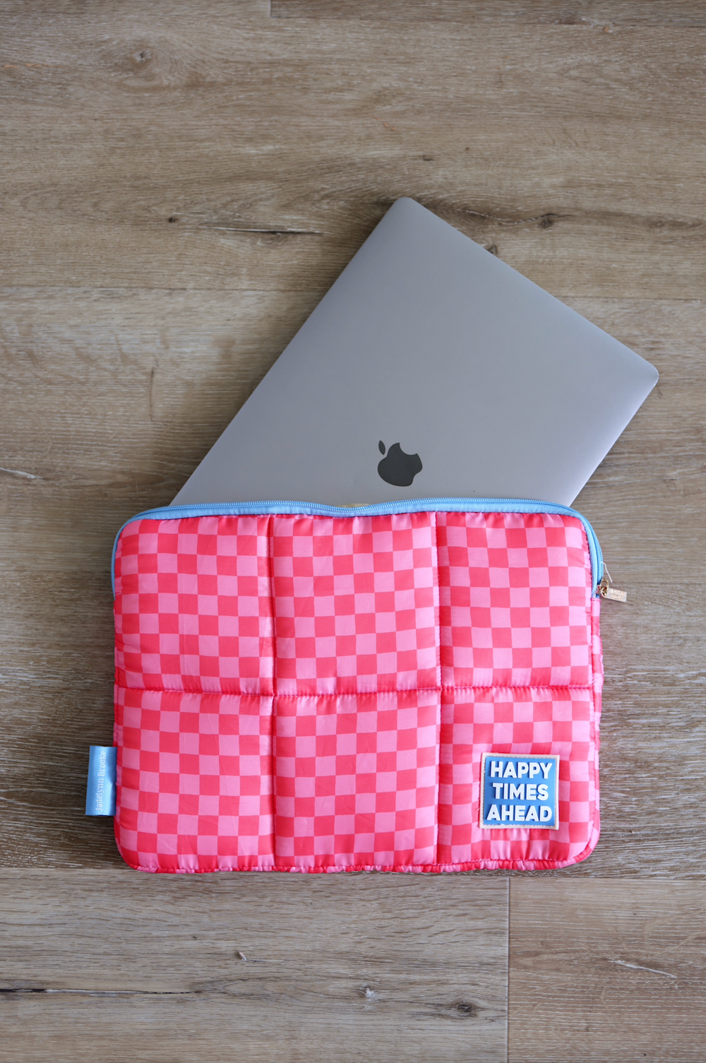 Pink checkered laptop sleeve with padded design, featuring 'Happy Times Ahead' patch and blue zipper.