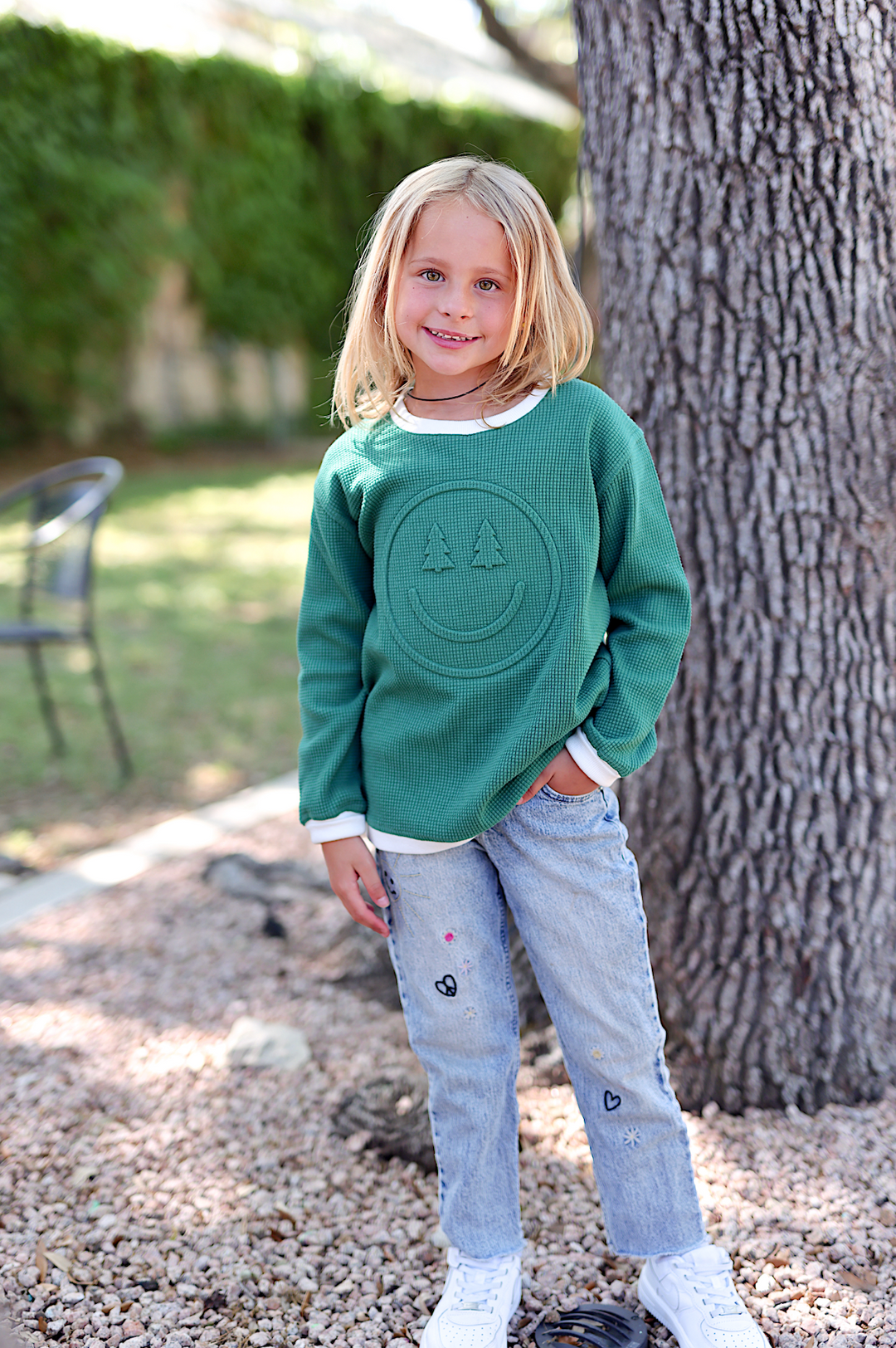 Kids' green waffle knit sweatshirt with smiley face design, paired with light blue embroidered jeans.