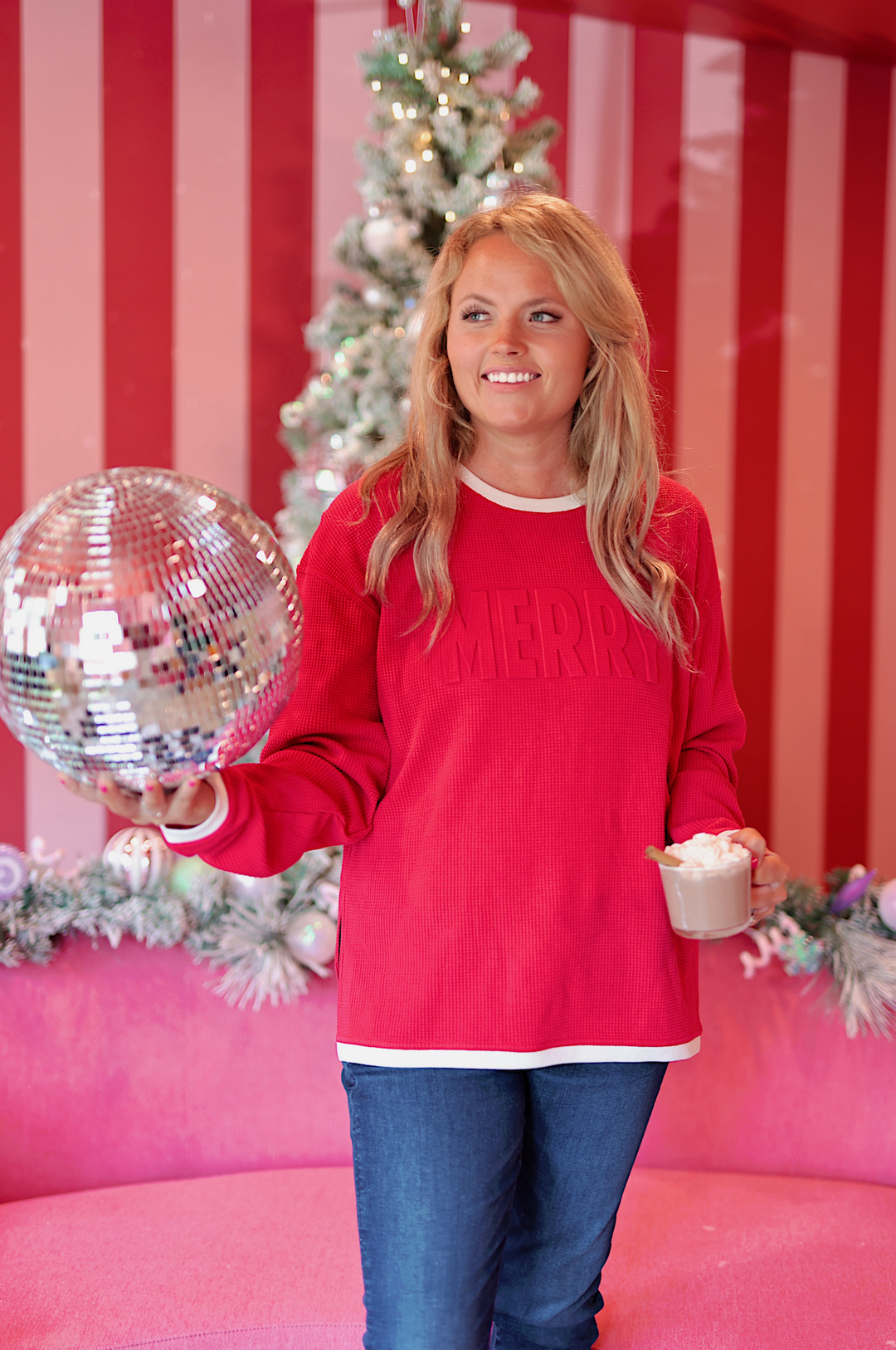 Cozy red 'MERRY' sweater in waffle knit, paired with jeans, festive backdrop with Christmas tree.