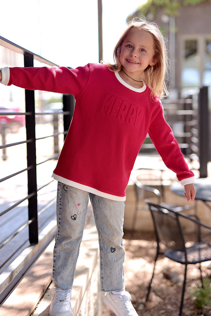 Kids' red Merry sweater in waffle knit, paired with embroidered denim jeans and white sneakers.