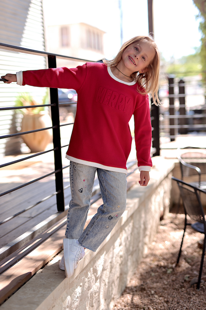 Red plush 'MERRY' sweatshirt for kids with white trim, paired with embroidered light denim jeans.