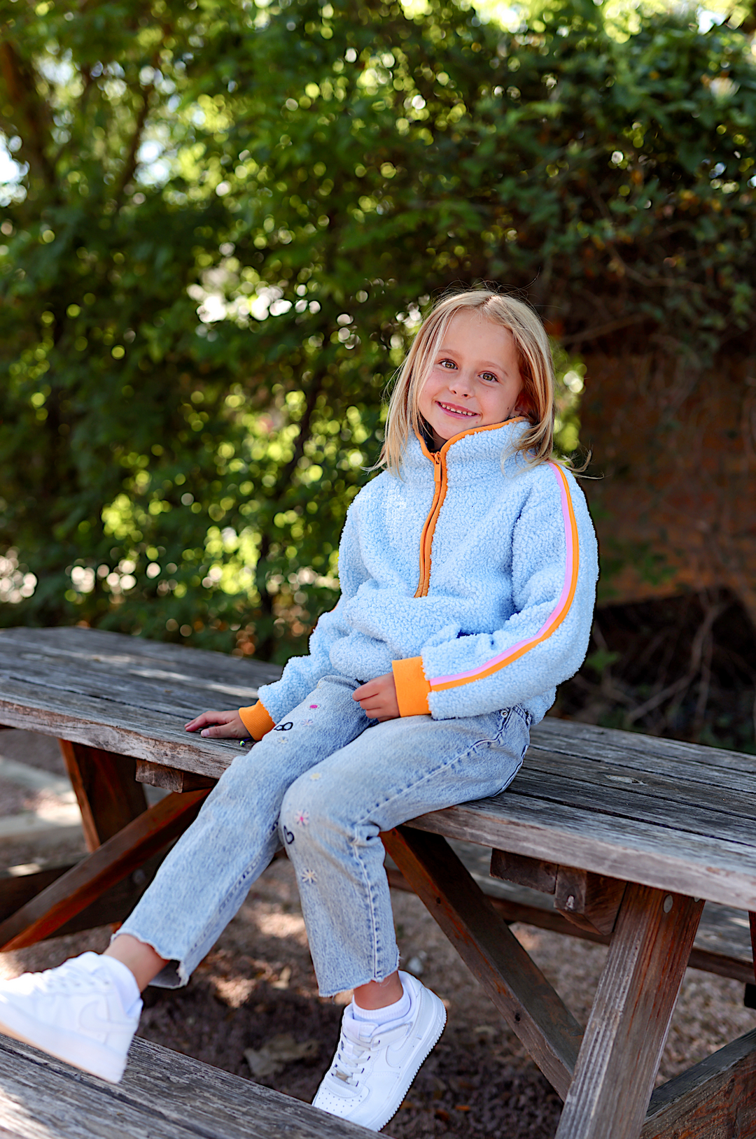 Light blue fleece jacket with orange accents, perfect for kids, styled with denim jeans and white sneakers.