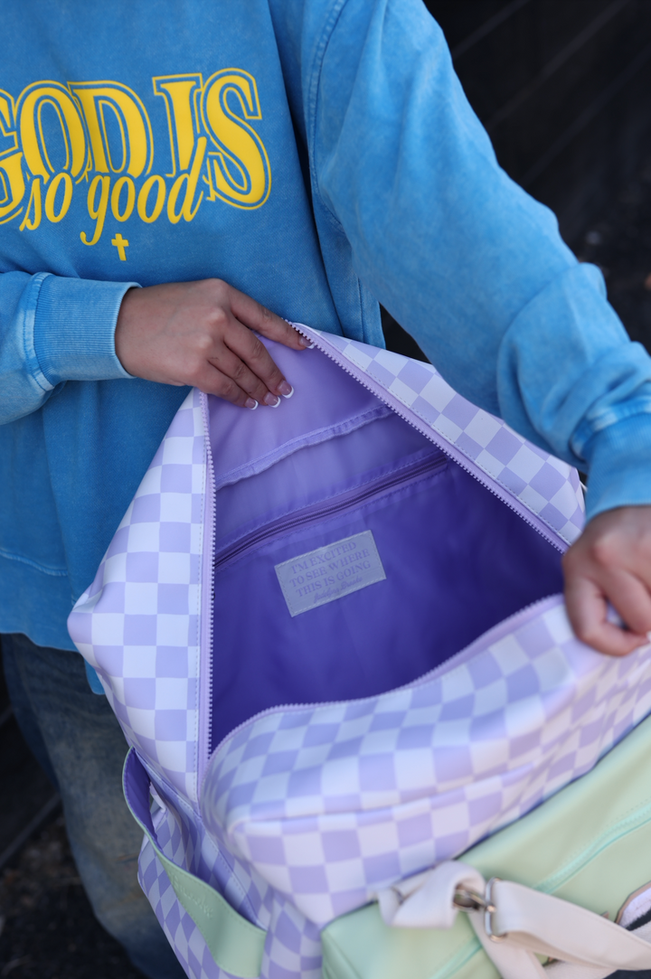 Colorful checkered bag with lavender interior and motivational label, perfect for stylish travel.
