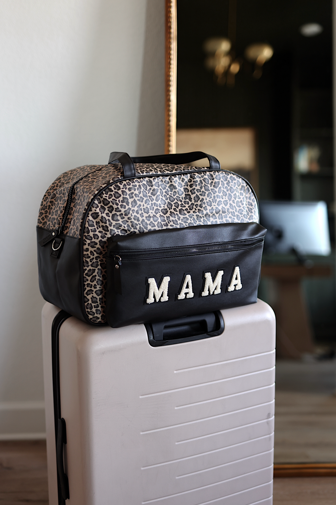 Leopard print duffel bag labeled 'MAMA' on top of a suitcase indoors.