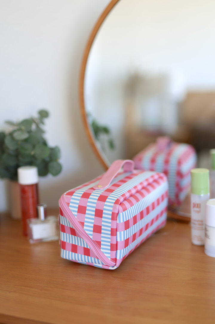 Colorful striped cosmetic bag in pink, blue, and white PVC with a sturdy handle for travel and organization.