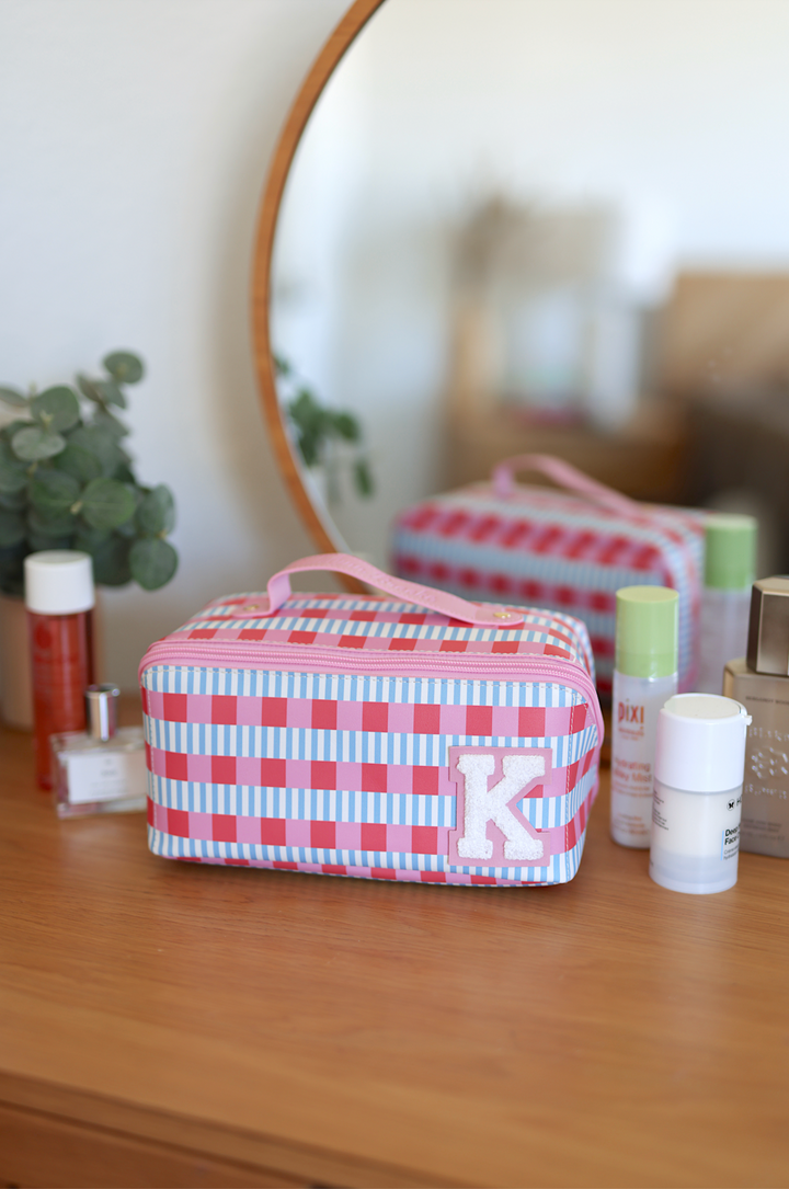 Colorful striped makeup bag with a pink handle and initial 'K', perfect for travel and organization.