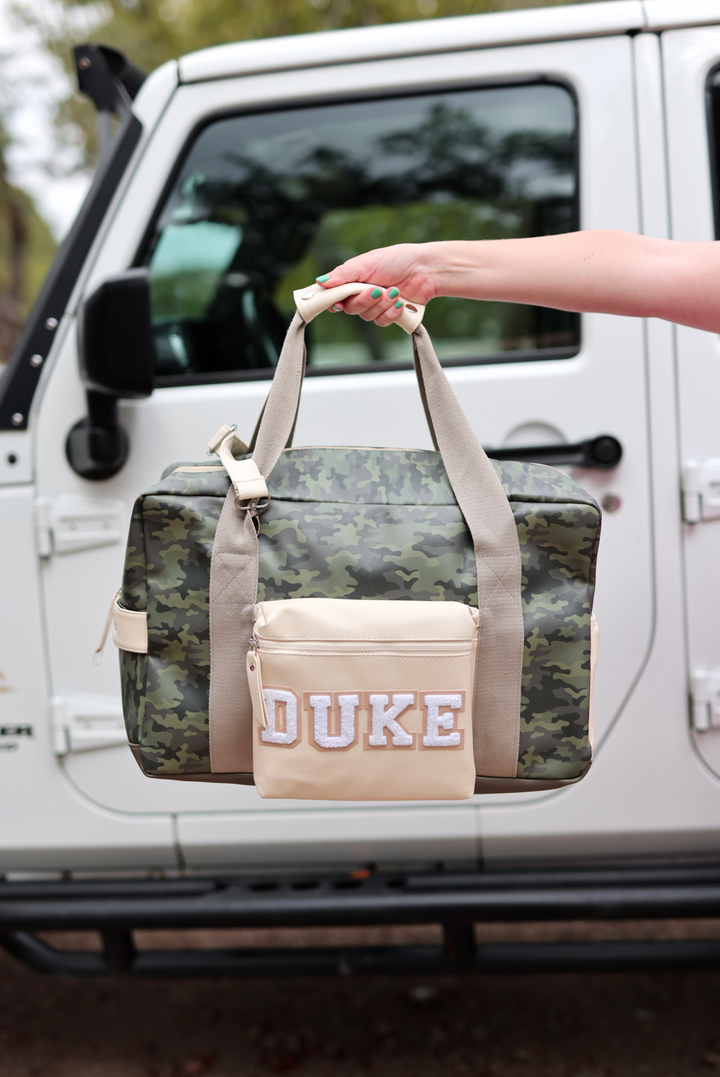 Camouflage duffel bag with cream pocket featuring 'DUKE' text, perfect for travel or gym.