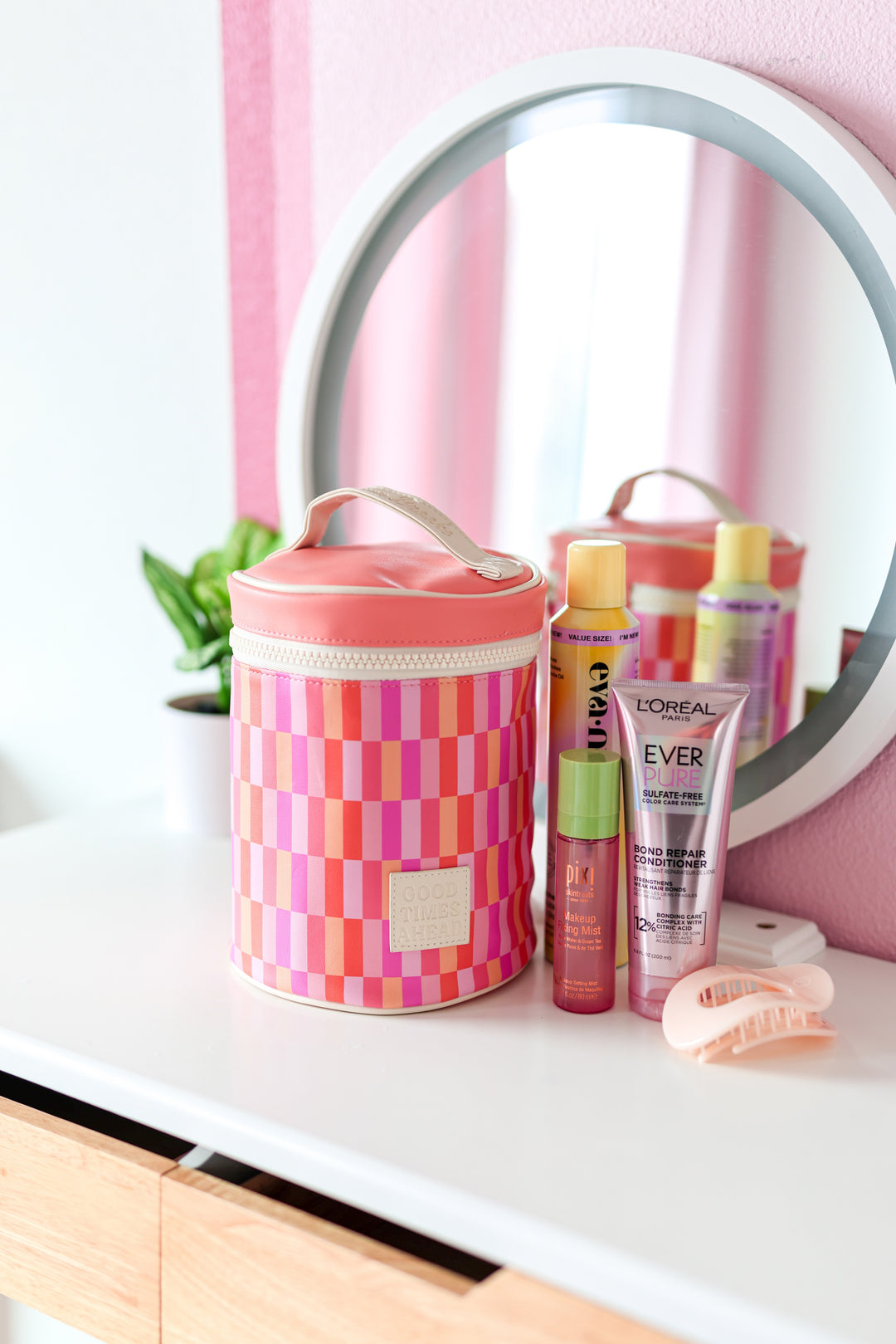 Colorful pink and orange checkered cosmetic bag with beauty products on a white vanity.