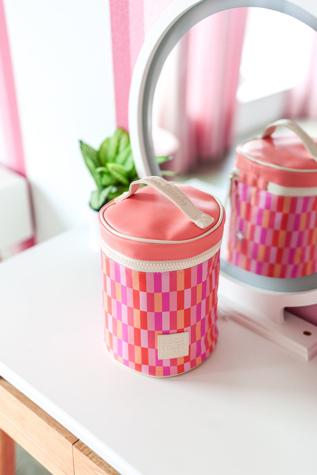 Colorful round cosmetic bag in pink and orange checker pattern, made of durable material with zipper closure.