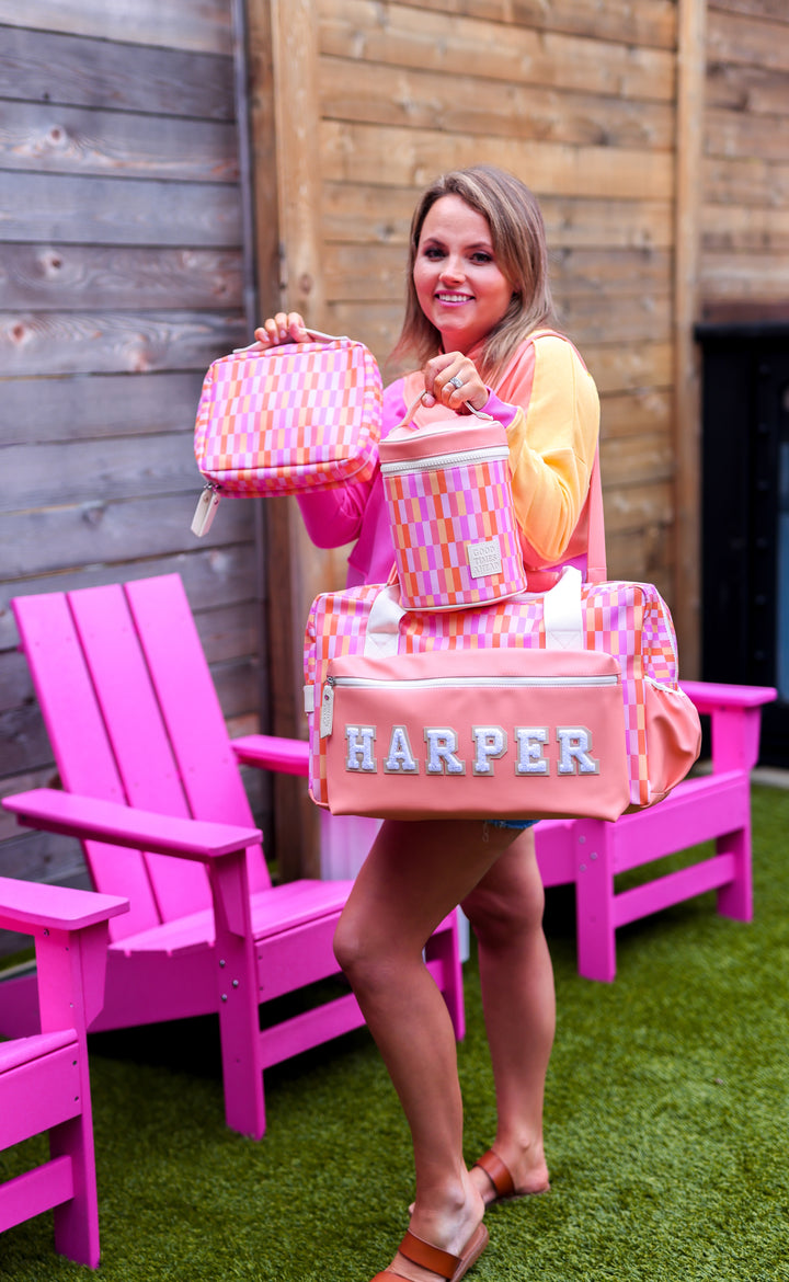 Colorful pink checkered travel bag set including duffel, lunchbox, and matching pouch.