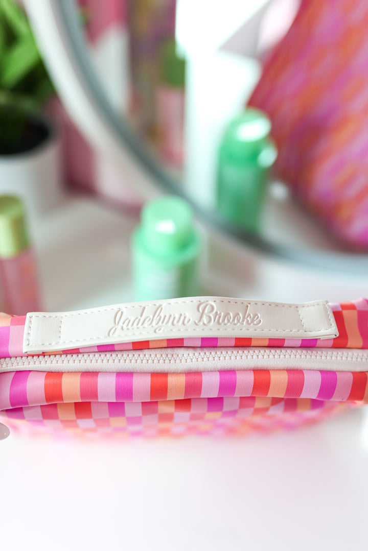 Colorful striped makeup bag in pink and orange with white leather label by Jadebryn Brooke.