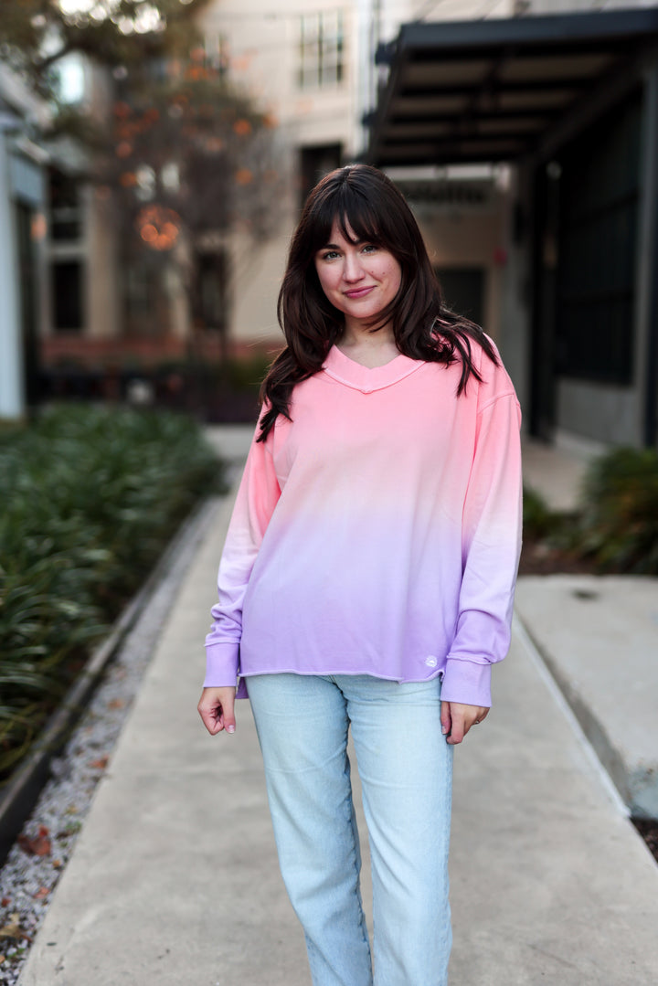 Woman wearing a gradient sweatshirt standing on a sidewalk with blurred background