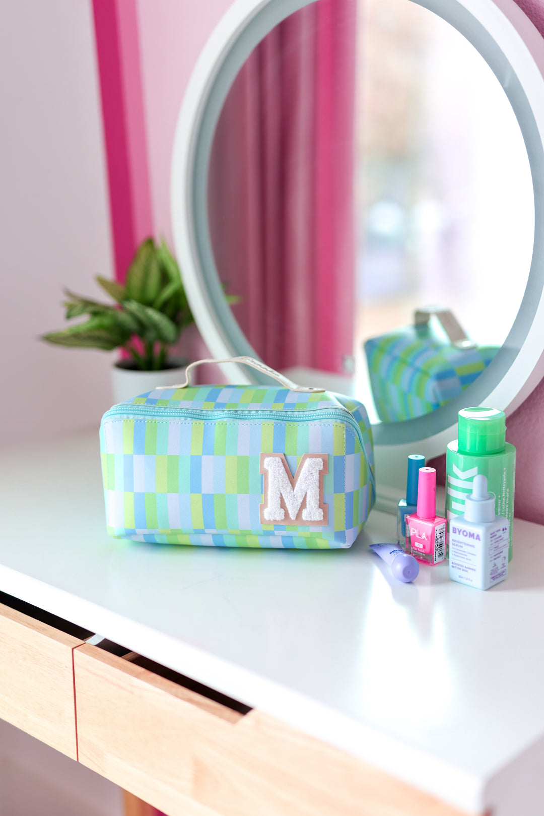 Colorful blue and green checkered makeup bag with plush 'M' monogram, perfect for cosmetics storage.