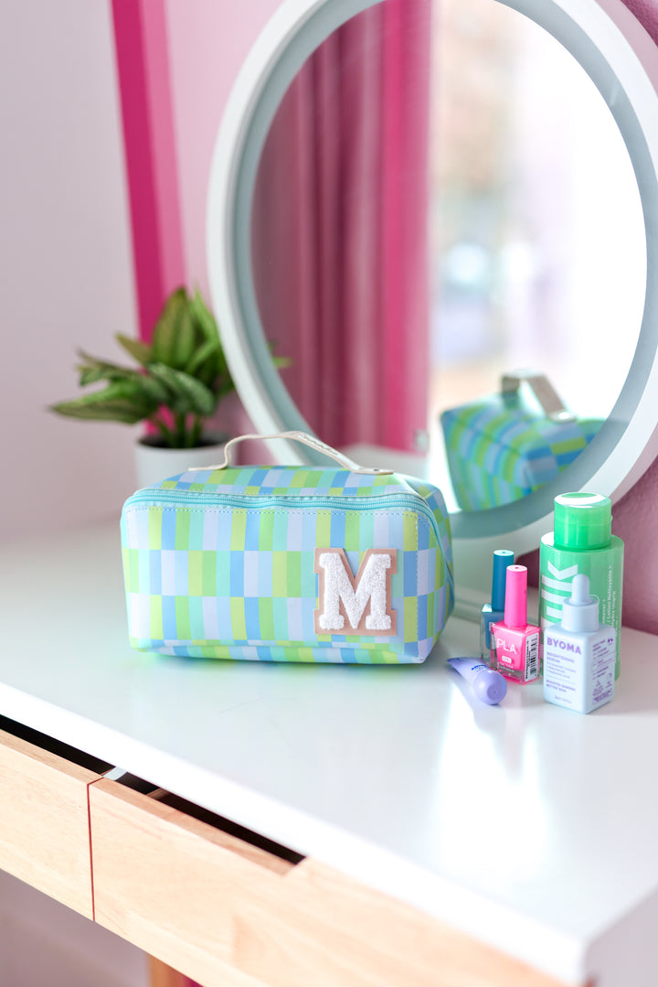 Colorful blue and green checkered makeup bag with plush 'M' monogram, perfect for cosmetics storage.