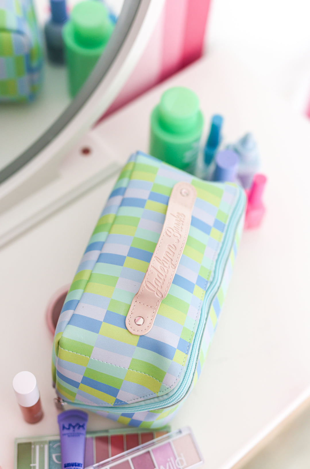 Colorful plaid makeup bag in blue and green, featuring a leather name tag and zipper closure, ideal for cosmetics.