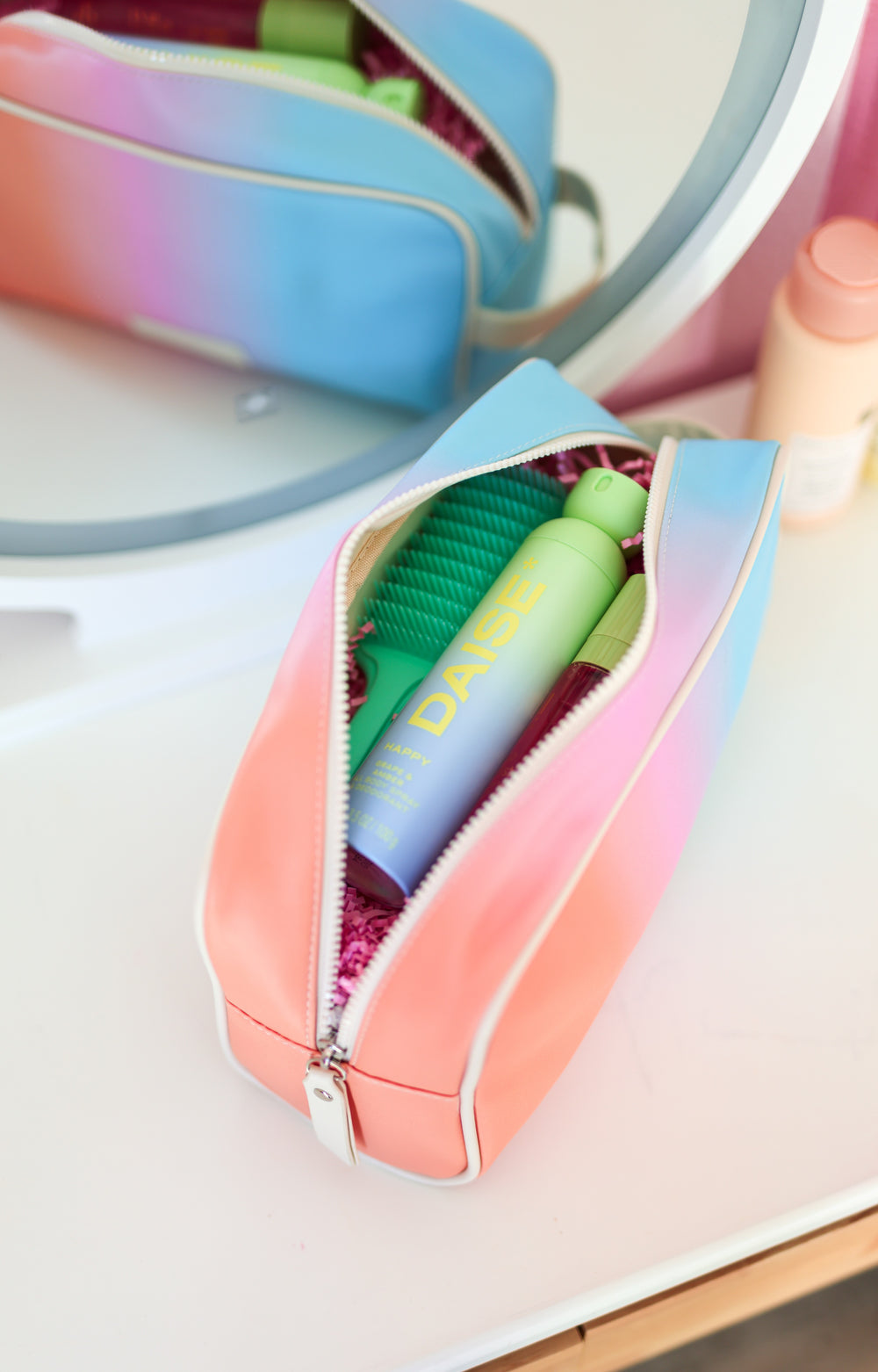 Colorful makeup brush set in a gradient case with a mirror in the background.