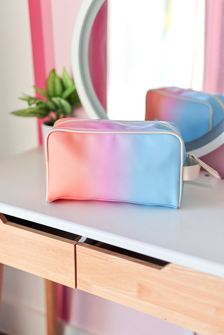 Gradient-colored makeup bag on a vanity table with a mirror and plant in the background